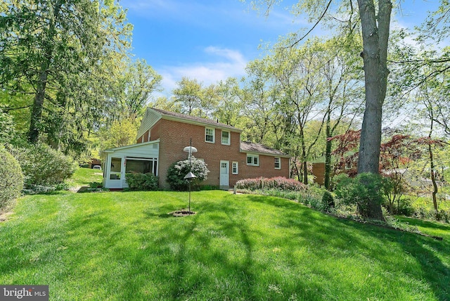 back of property featuring a yard, brick siding, and a sunroom