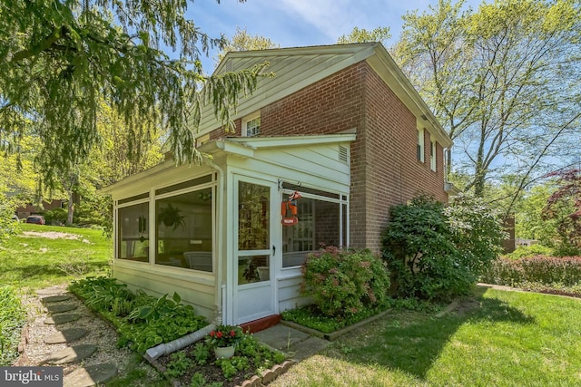 view of side of property with brick siding, a lawn, and a sunroom