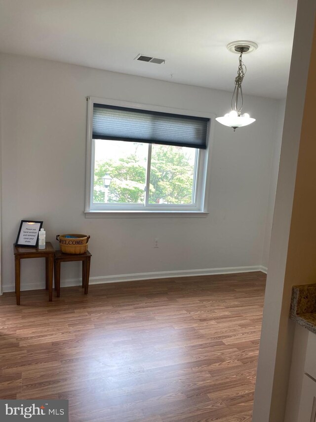 unfurnished dining area featuring baseboards, visible vents, and wood finished floors