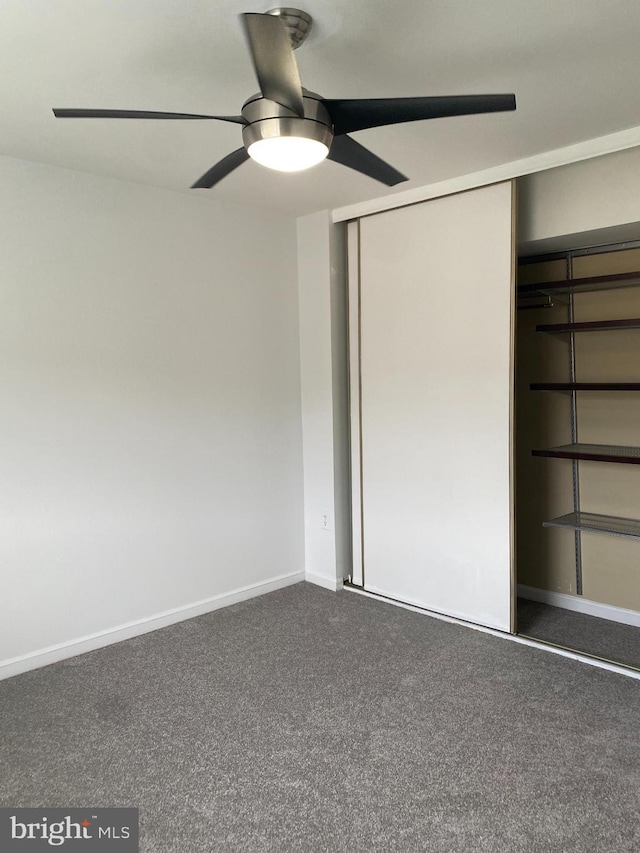 unfurnished bedroom with baseboards, ceiling fan, dark carpet, and a closet