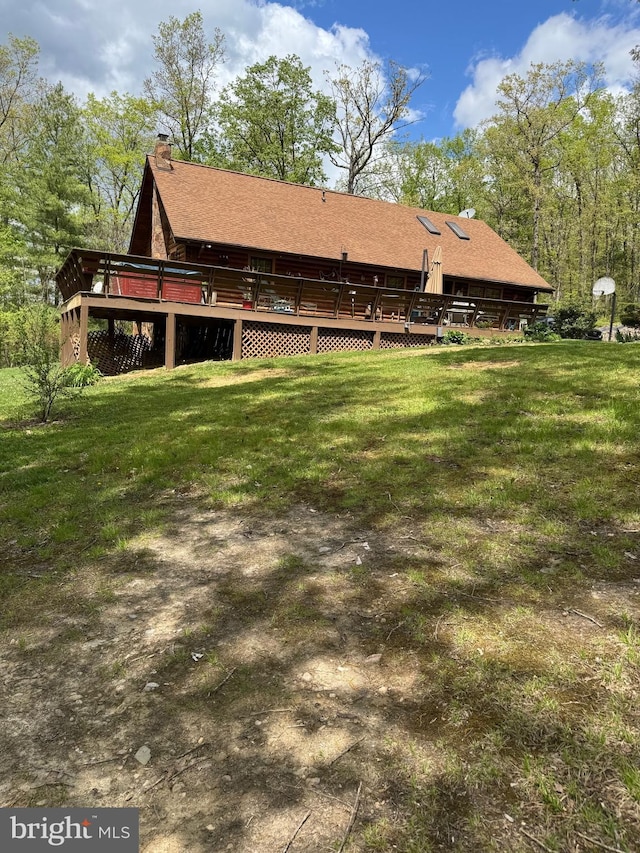 back of house with a lawn, roof with shingles, a wooden deck, and a chimney