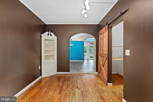interior space featuring a textured ceiling, baseboards, a barn door, and wood finished floors