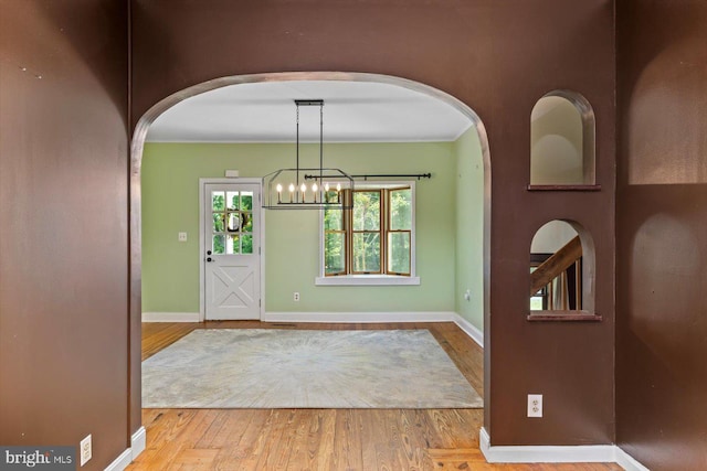 foyer entrance featuring arched walkways, baseboards, wood finished floors, and a notable chandelier