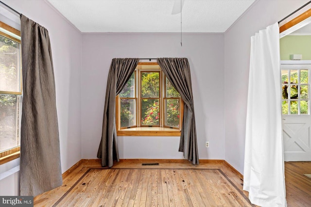unfurnished room with wood-type flooring, a ceiling fan, baseboards, and a healthy amount of sunlight