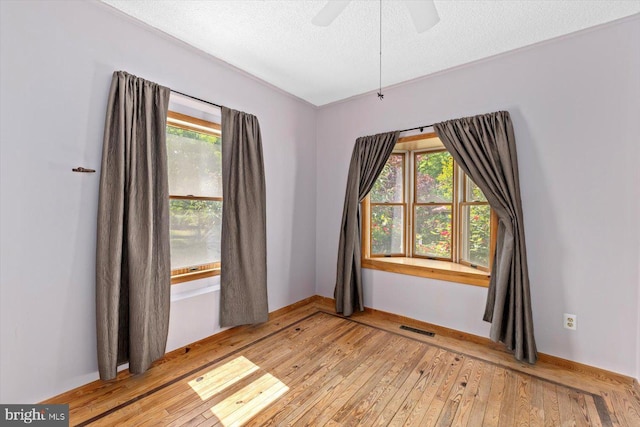 spare room featuring light wood finished floors, a textured ceiling, a ceiling fan, baseboards, and visible vents