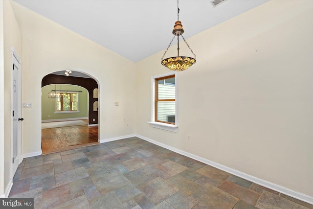 unfurnished dining area featuring stone tile flooring, arched walkways, baseboards, and a notable chandelier