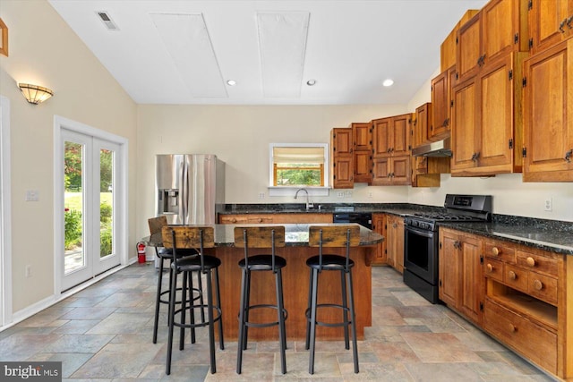 kitchen featuring a breakfast bar, stone tile floors, stainless steel appliances, and under cabinet range hood