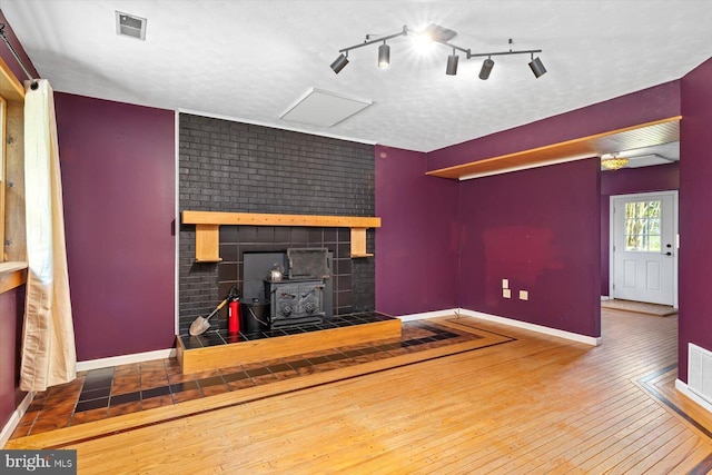 unfurnished living room featuring baseboards, a wood stove, hardwood / wood-style flooring, and visible vents