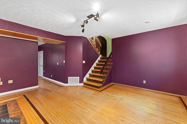 interior space featuring wood-type flooring, stairs, baseboards, and visible vents