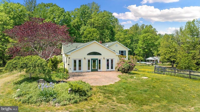 rear view of property featuring fence, a patio, french doors, a lawn, and a forest view