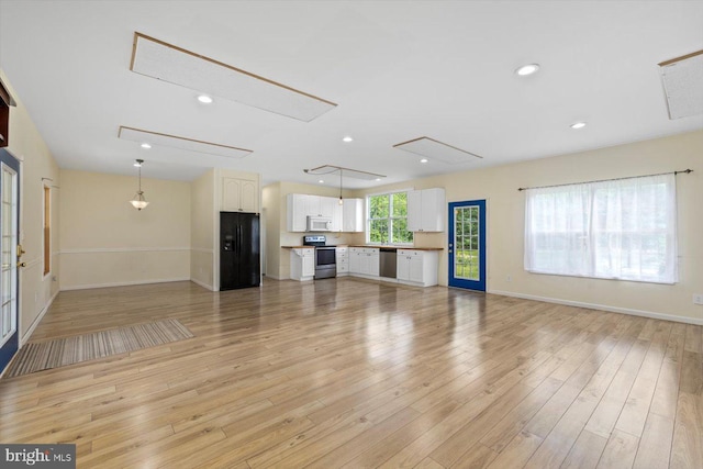 unfurnished living room with baseboards, attic access, and light wood-style floors
