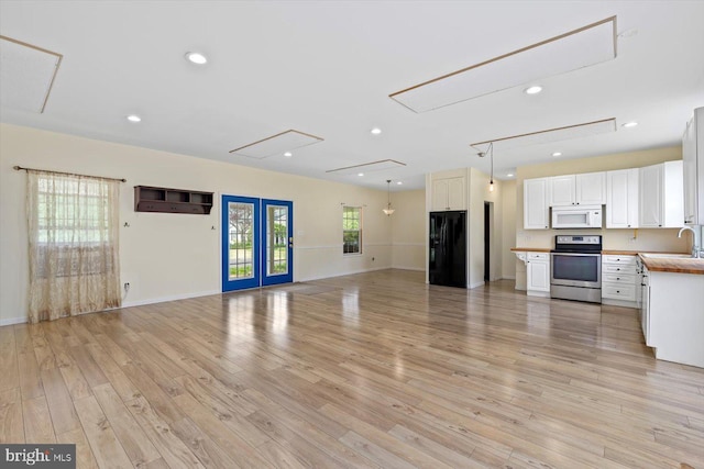 unfurnished living room featuring baseboards, a sink, light wood finished floors, and attic access