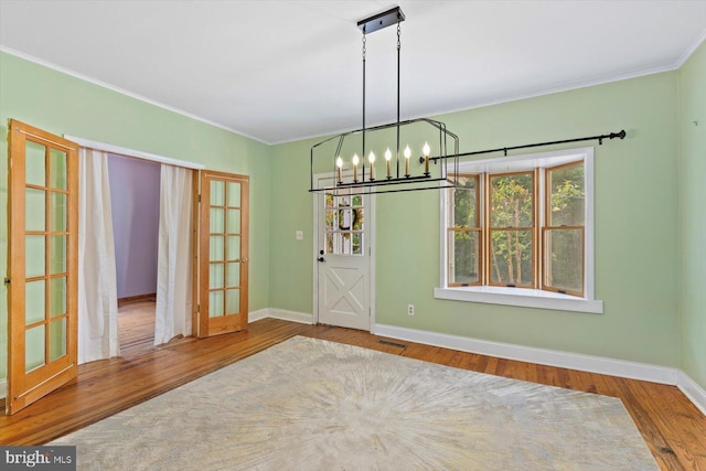 unfurnished dining area featuring crown molding, a chandelier, baseboards, wood finished floors, and visible vents