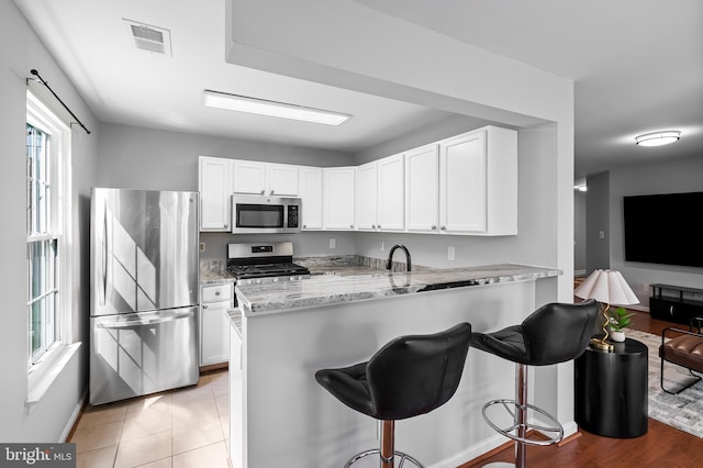 kitchen featuring a kitchen breakfast bar, appliances with stainless steel finishes, light stone countertops, a peninsula, and white cabinetry