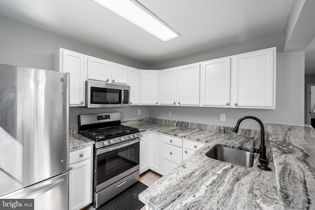 kitchen featuring white cabinets, light stone countertops, appliances with stainless steel finishes, and a sink