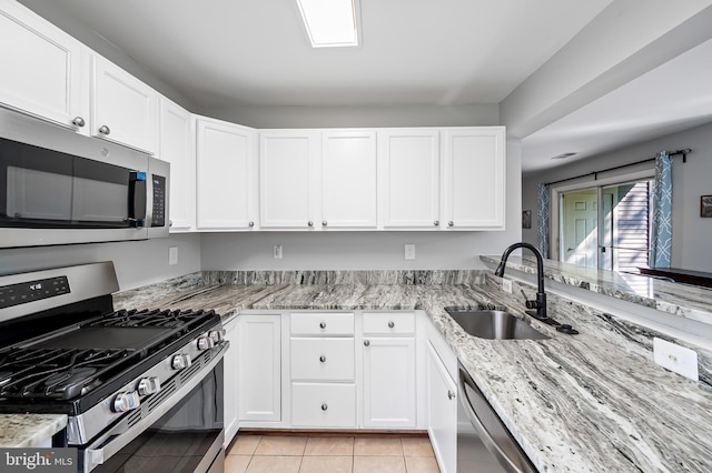 kitchen with a sink, light stone counters, light tile patterned floors, and stainless steel appliances