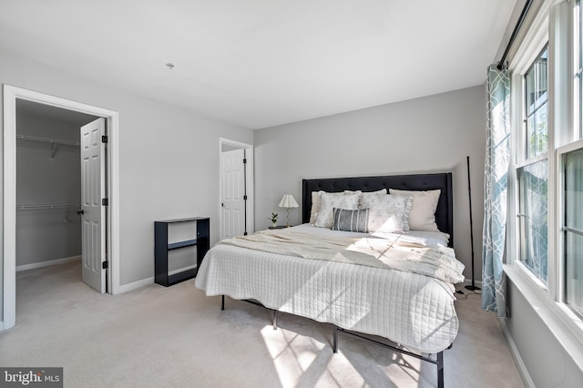 bedroom featuring baseboards, a walk in closet, a closet, and light carpet