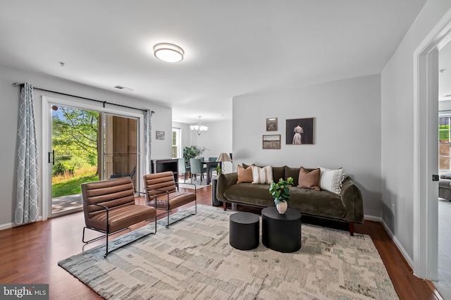 living room featuring baseboards, visible vents, wood finished floors, and a notable chandelier