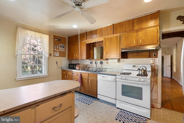 kitchen featuring light countertops, under cabinet range hood, brown cabinets, and white appliances