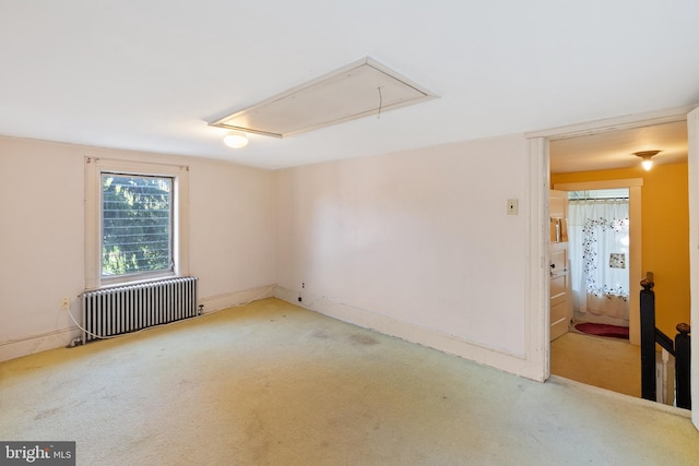 empty room with carpet floors, baseboards, radiator heating unit, and attic access