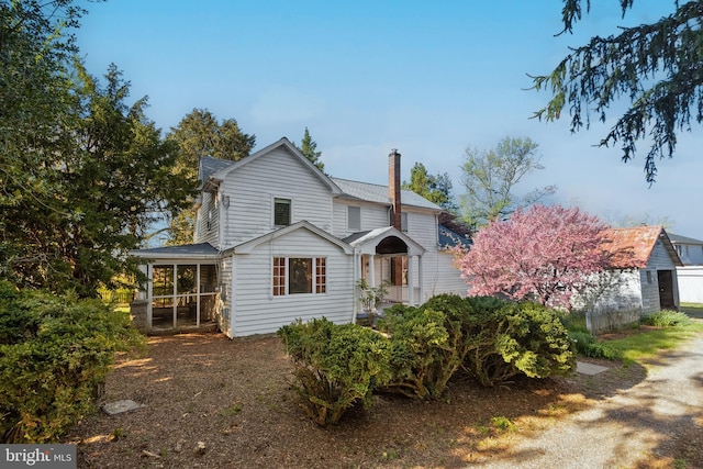 traditional-style home featuring a sunroom, roof with shingles, and a chimney