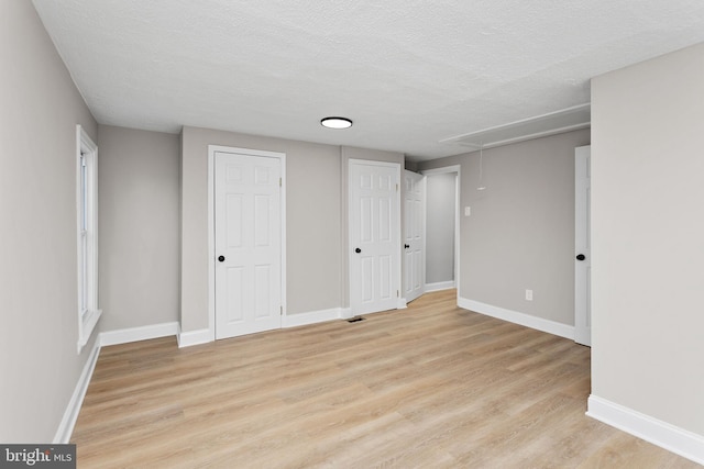 unfurnished bedroom with light wood finished floors, a textured ceiling, attic access, baseboards, and visible vents