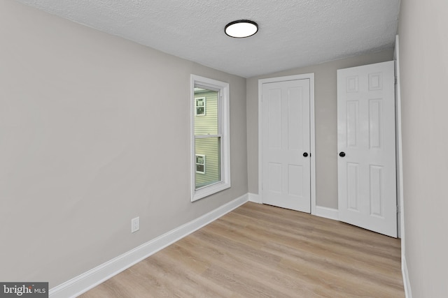 unfurnished bedroom featuring light wood-type flooring, a textured ceiling, baseboards, and a closet