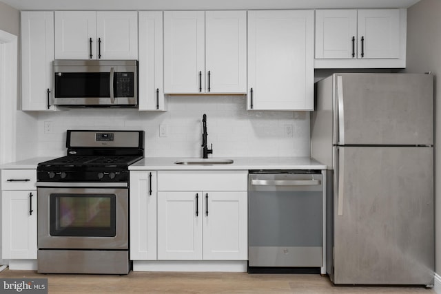 kitchen with backsplash, a sink, light countertops, white cabinets, and stainless steel appliances