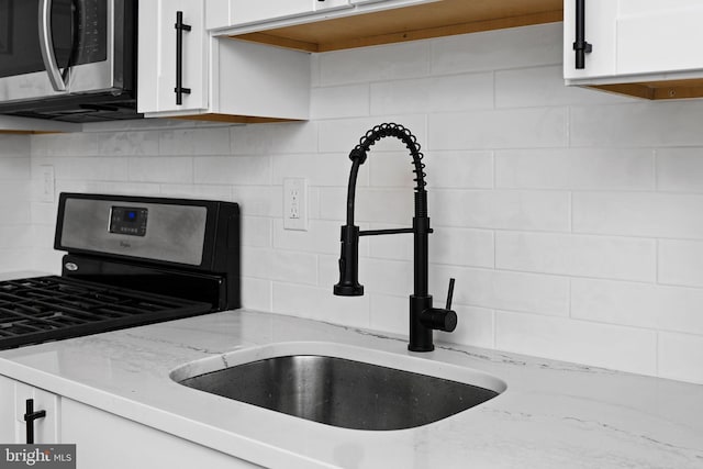 room details with a sink, tasteful backsplash, stainless steel appliances, and white cabinetry