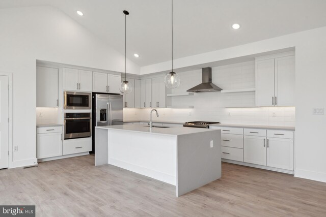 kitchen with backsplash, appliances with stainless steel finishes, a sink, light countertops, and wall chimney exhaust hood