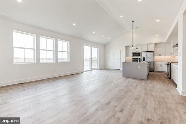 kitchen with appliances with stainless steel finishes, high vaulted ceiling, open floor plan, visible vents, and a center island with sink