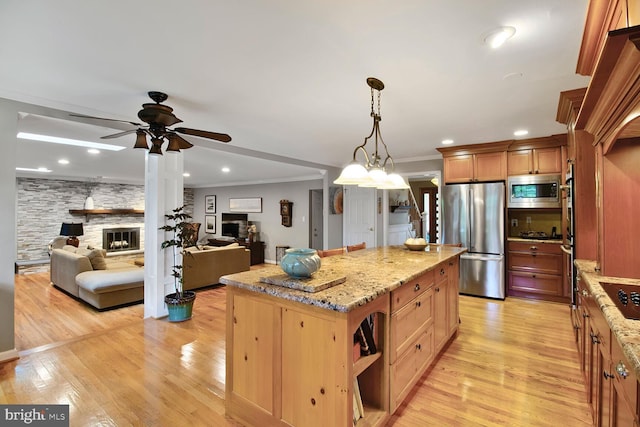 kitchen with a ceiling fan, light stone counters, a kitchen island, a fireplace, and appliances with stainless steel finishes