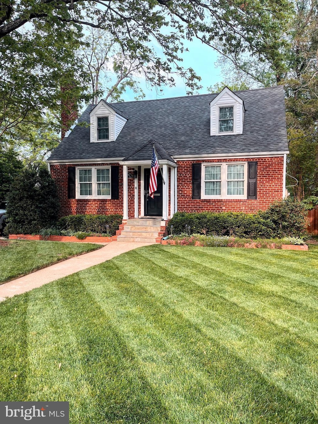 cape cod-style house with brick siding and a front lawn