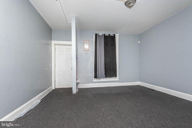unfurnished room with dark carpet and baseboards