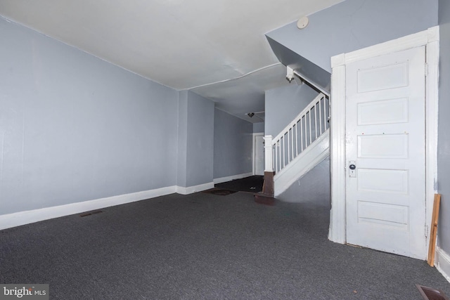 unfurnished living room with visible vents, baseboards, dark carpet, and stairway