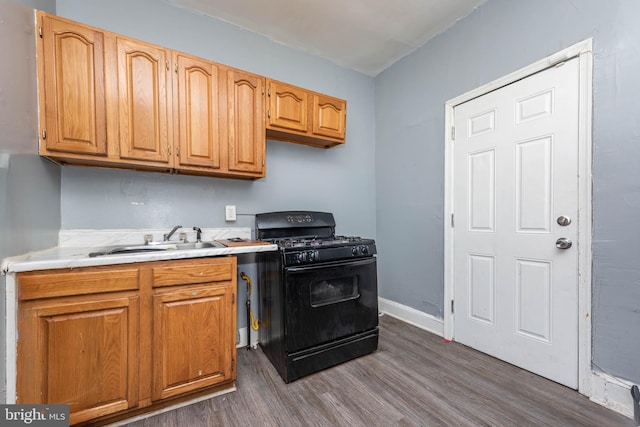 kitchen with black gas stove, a sink, dark wood finished floors, and light countertops