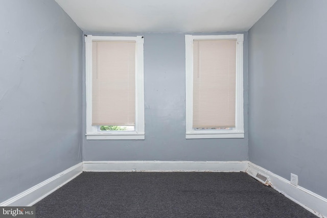 unfurnished room with baseboards, visible vents, and dark carpet