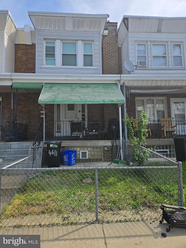 townhome / multi-family property with covered porch, brick siding, and a fenced front yard