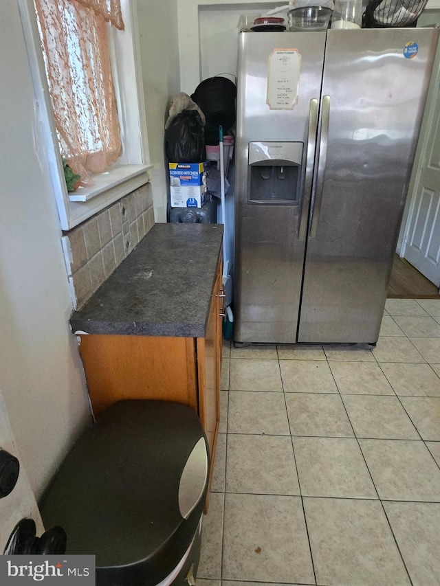 kitchen with dark countertops, tasteful backsplash, brown cabinets, stainless steel fridge with ice dispenser, and light tile patterned flooring
