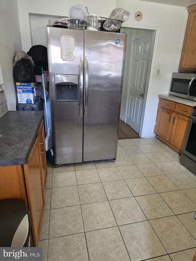 kitchen with brown cabinets, stainless steel appliances, dark countertops, and light tile patterned floors