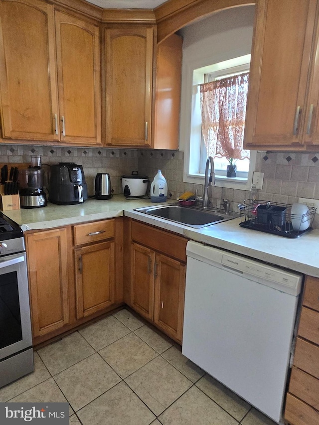 kitchen featuring stainless steel electric range, a sink, dishwasher, light countertops, and light tile patterned floors