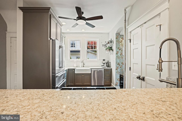 kitchen featuring a sink, stainless steel appliances, arched walkways, a ceiling fan, and gray cabinetry