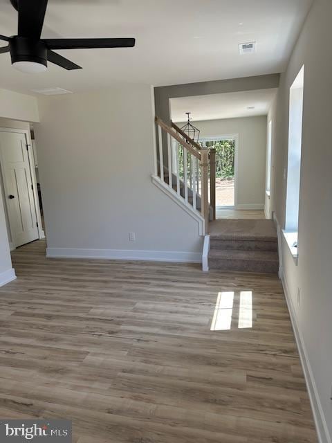 unfurnished living room with visible vents, wood finished floors, stairway, baseboards, and ceiling fan with notable chandelier