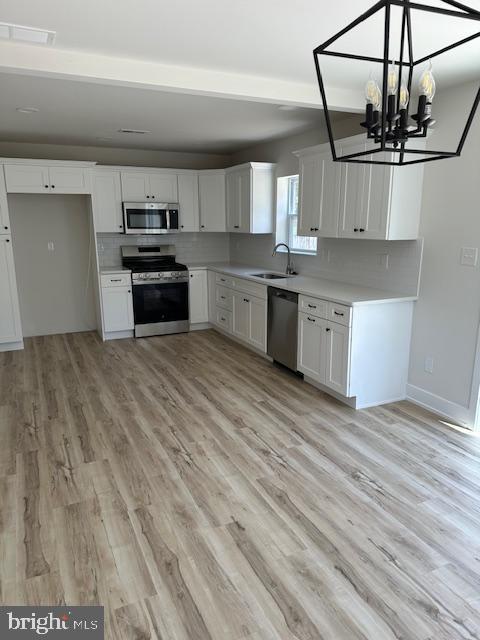 kitchen with a sink, white cabinets, stainless steel appliances, and light wood-style flooring