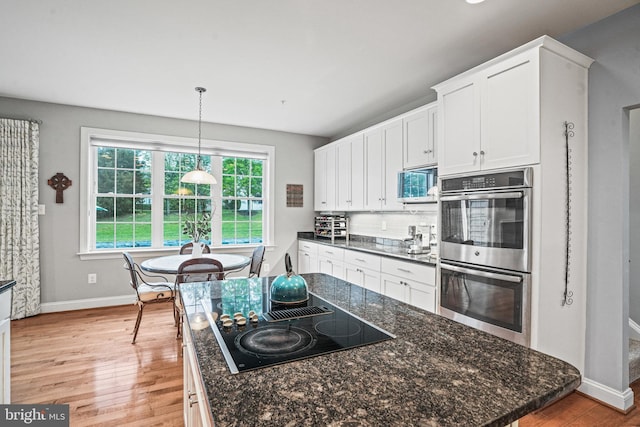 kitchen with light wood-style flooring, stainless steel double oven, white cabinetry, baseboards, and black electric stovetop