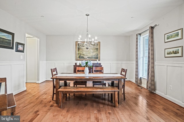 dining space with an inviting chandelier, light wood-style flooring, a decorative wall, and a wainscoted wall