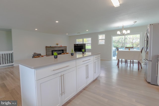kitchen featuring white cabinets, an inviting chandelier, light wood finished floors, a fireplace, and freestanding refrigerator