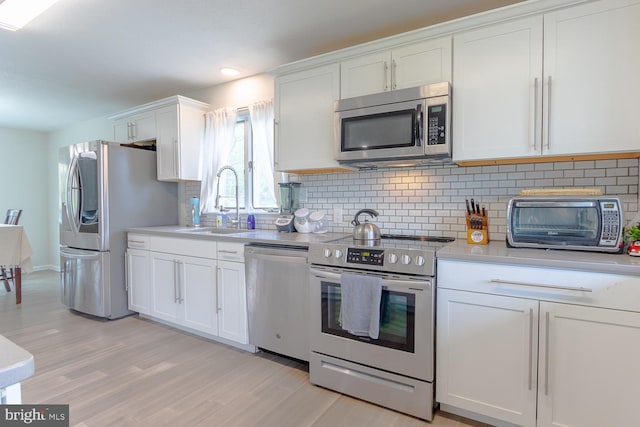 kitchen with backsplash, stainless steel appliances, white cabinetry, and a sink