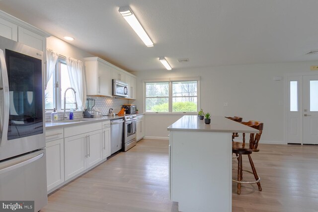 kitchen featuring a kitchen island, appliances with stainless steel finishes, a sink, a breakfast bar, and light wood-style flooring