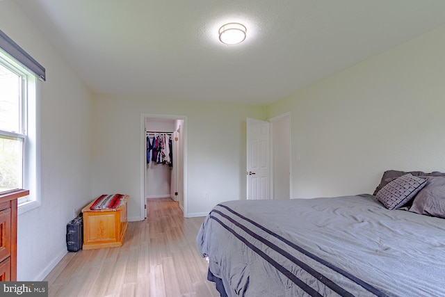 bedroom featuring light wood-type flooring, baseboards, a walk in closet, and a closet